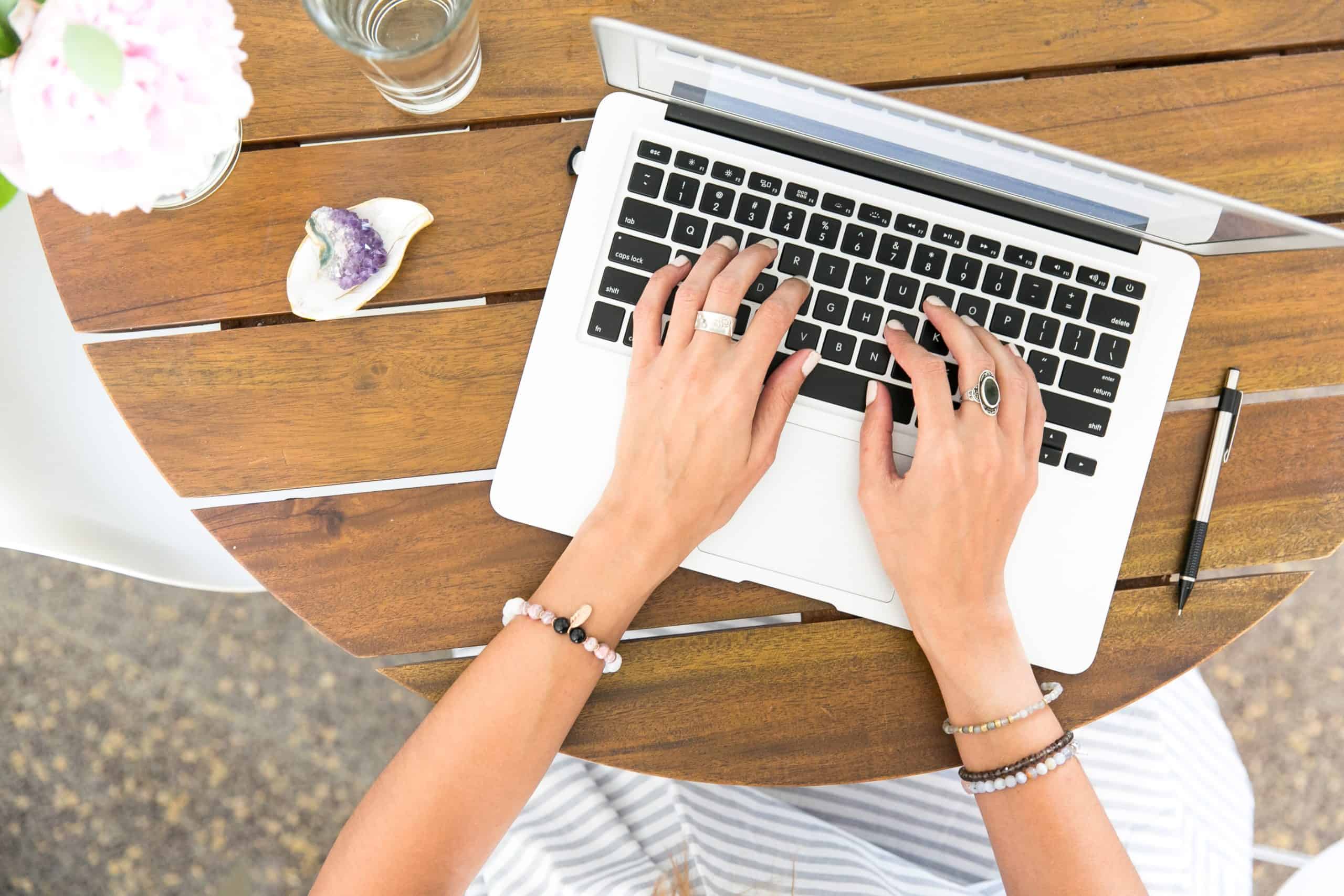 A person working on a laptop at an outdoor setting, with a clear glass of water and fresh flowers on the side.