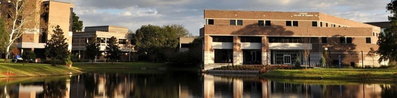 Tranquil waters mirror the clear skies in front of a modern academic building, encapsulating a serene campus atmosphere.