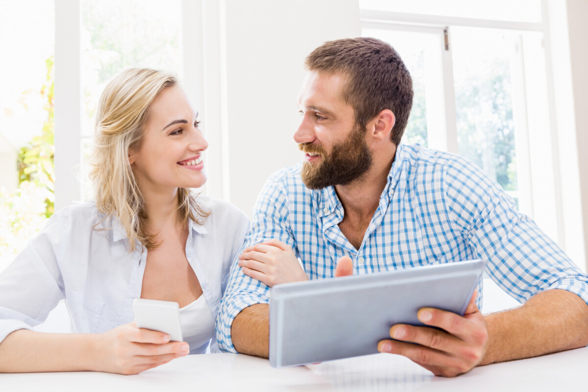 A smiling couple enjoying a moment together with a digital tablet and a credit card, possibly making an online purchase or planning something.