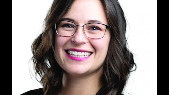 A woman with shoulder-length brown hair, wearing glasses and a black top, smiling at the camera against a white background.