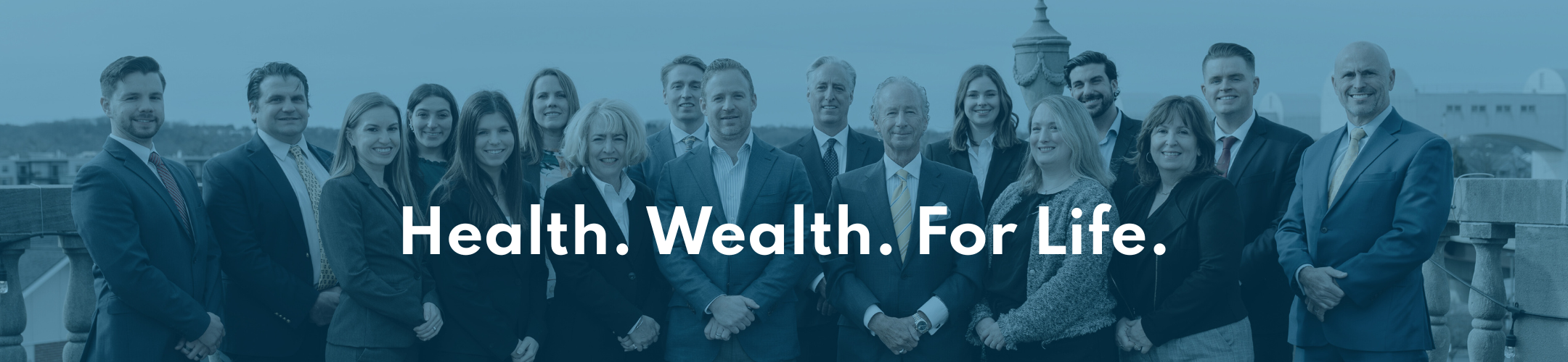 A group of professionally dressed people stand together outdoors, smiling at the camera. The text 